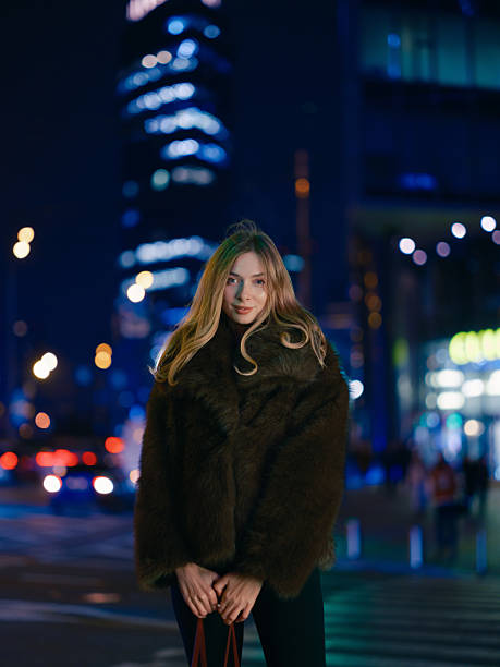 istock Stylish Woman Poses Fur Coat Modern Skyscraper Night 2251704242
