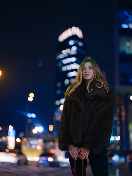 istock Stylish Woman Poses Fur Coat Modern Skyscraper Night 2251704251
