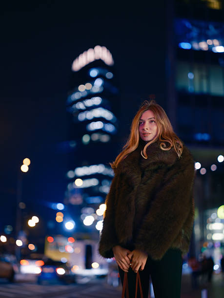 istock Stylish Woman Poses Fur Coat Modern Skyscraper Night 2251704253