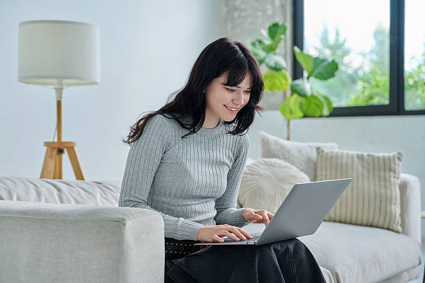 istock Young woman sitting on sofa typing on laptop, in home interior 2251709909