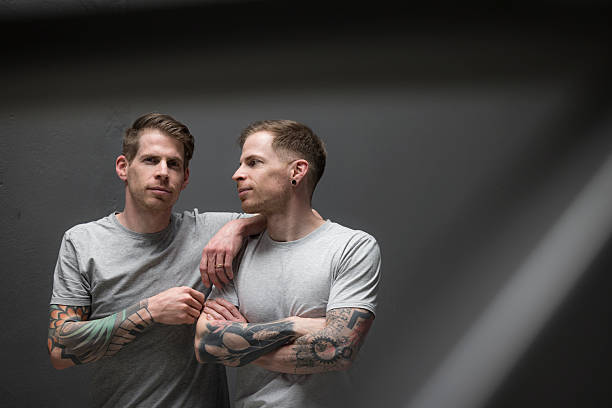 Two diverse young men are posing together with arms around each other, looking at the camera with a cool and friendly attitude in a studio shot against a gray background
