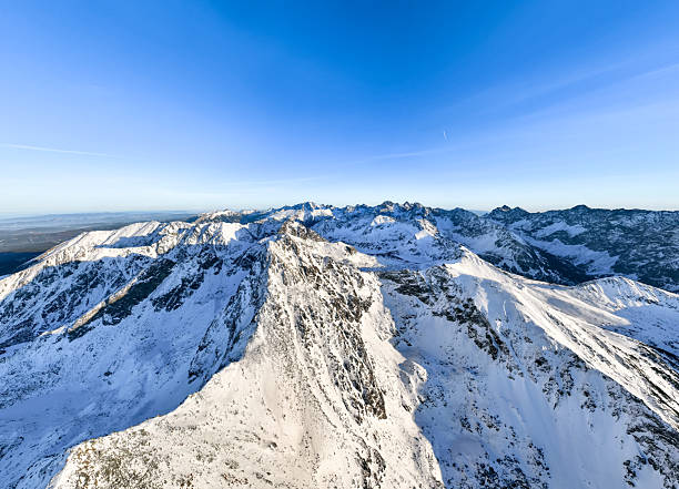 Snow-covered mountains stretch across the horizon with a clear blue sky above. Peaks rise sharply against the landscape in daylight.