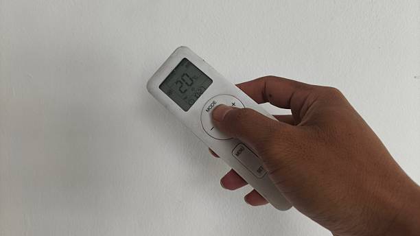 istock A hand holding a white air conditioner remote control with a plain white wall background. The remote display shows 20 degrees Celsius in cooling mode. Concept of home technology. 2251713410