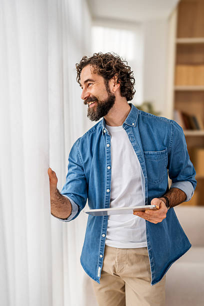 istock Man smiling holding tablet looking out window at home 2251716059