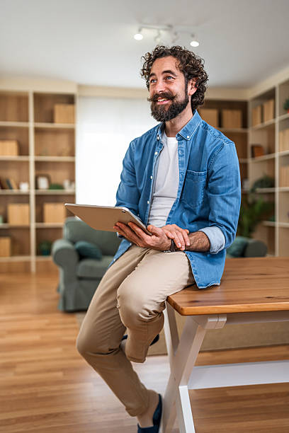 istock Man smiling holding tablet sitting on table at home 2251716075