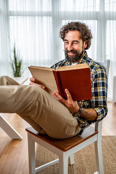istock Smiling man relaxing at home reading a book 2251716473