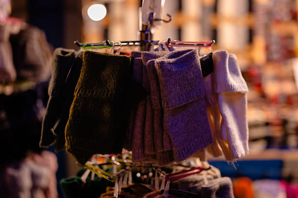 Close-up view of warm knitted wool gloves hanging on a rack at a Berlin Christmas market, captured during the winter holiday season with festive night lighting. Ideal for themes of winter fashion, handmade goods, and holiday shopping.