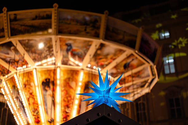 A glowing blue Christmas star sits above a market stall with a vintage carousel glowing warmly in the background.
