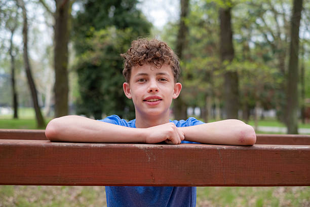 Teenager boy smiling in a park, leaning on a wooden structure