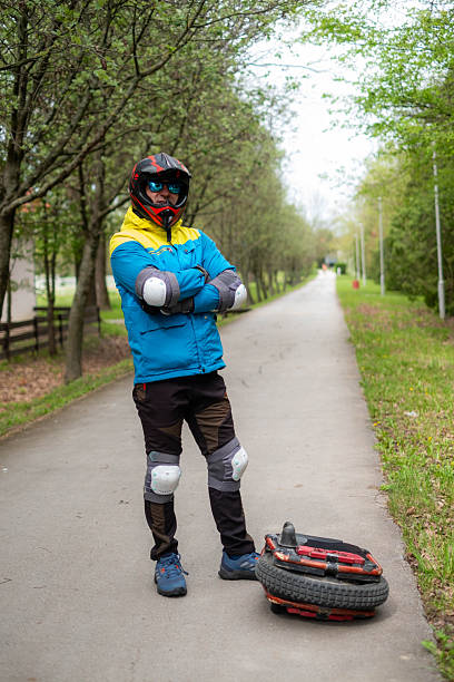 Man in helmet and pads standing on a path next to an electric unicycle
