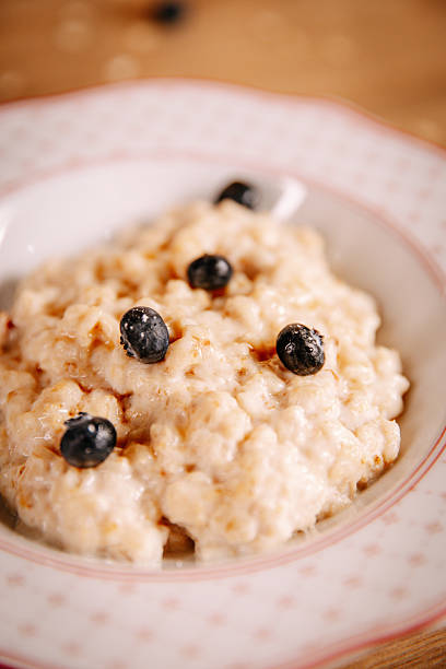 Close-up of creamy oatmeal porridge topped with blueberries, served in ceramic bowl. Warm homemade breakfast with soft light and calm healthy lifestyle mood.
