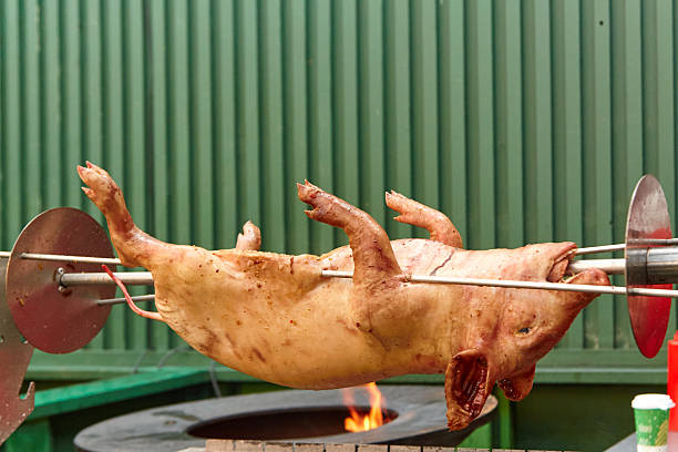 Whole pig is being roasted on a spit over an open flame, highlighting traditional cooking methods and the vibrant outdoor culinary experience