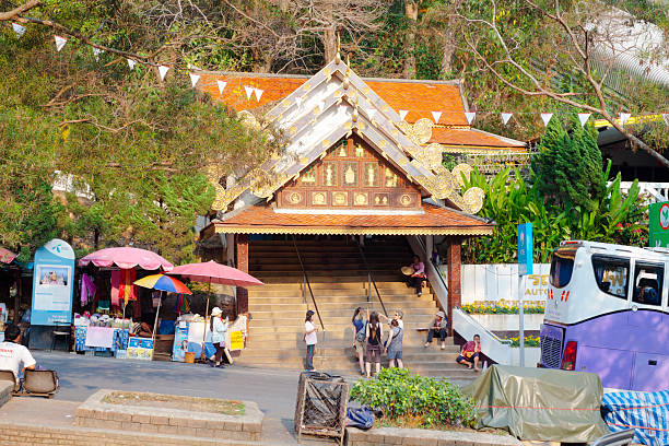 Gate and steps to Doi Suthep in Chiang Mai.  Wat Phra Doi Suthep in outskirts of Chiang Mai, international landmark high up on mountain. Temple is built in early 19th century. At steps some white female tourists are standing and talking. Around are some thai women and vendors. At lelft side are food and souvenir market stalls