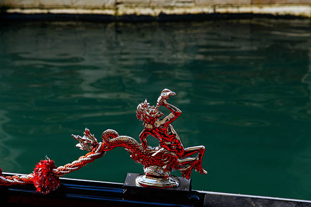 Venice, Italy - December 05, 2025: Red dragon sculpture on boat railing, reflecting in calm water, highlighting artistic detail and cultural heritage