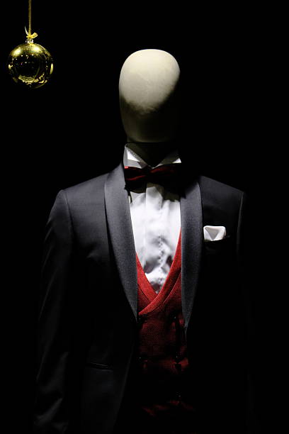 Studio-style image of a headless mannequin dressed in an elegant tuxedo with white shirt, red waistcoat, bow tie, and pocket square, isolated against a black background with dramatic lighting and ample copy space.