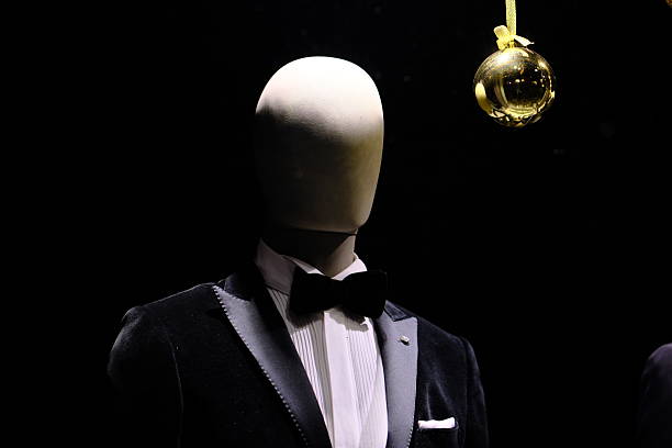 Studio-style image of a headless mannequin dressed in an elegant tuxedo with white shirt, red waistcoat, bow tie, and pocket square, isolated against a black background with dramatic lighting and ample copy space.