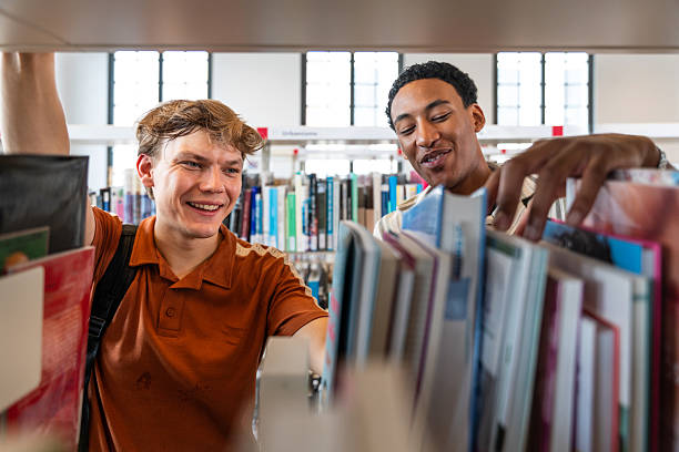 istock Two smiling students searching books in library shelves 2251743742