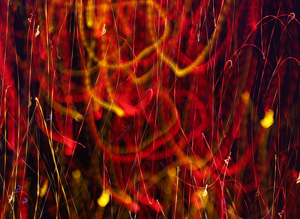 Vertical abstract light painting creates a rich and dynamic background featuring fiery red and golden-yellow light trails. Long exposure captures a multitude of intertwined lines and spots, mimicking an energy burst or chaotic nightlife.
