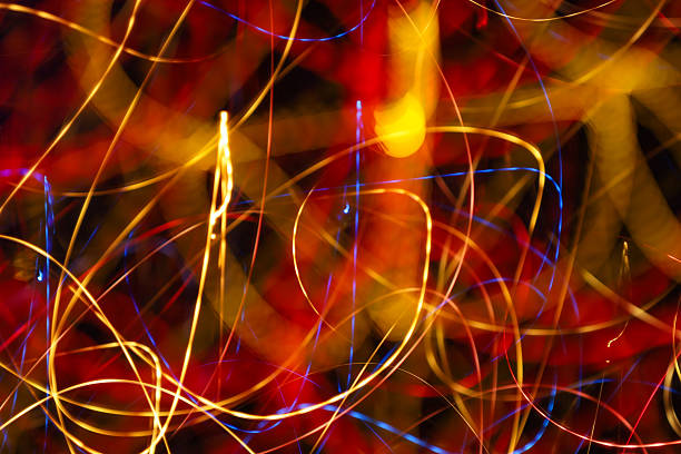 Abstract light painting creates a dynamic pattern of tangled golden, red, and blue light trails. Long exposure photography transforms bright night lights into an energetic, futuristic background perfect for design or cover art.