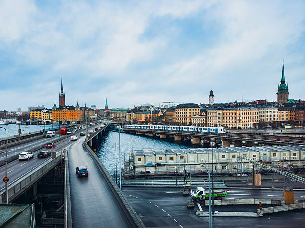 Editorial image of Centralbron road and metro bridge in Stockholm, Sweden, with historic Gamla Stan skyline in the background. Photo taken on December 1st, 2025. Cars, train, water and old buildings under cloudy winter sky. Editorial use only.