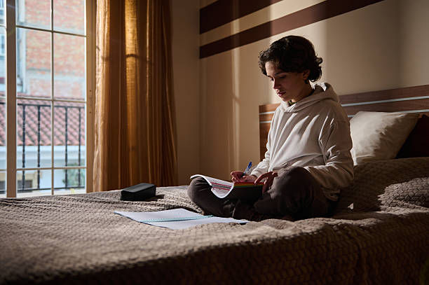 istock Young Man Studying on Bed by Window With Notebook and Pens 2251751715