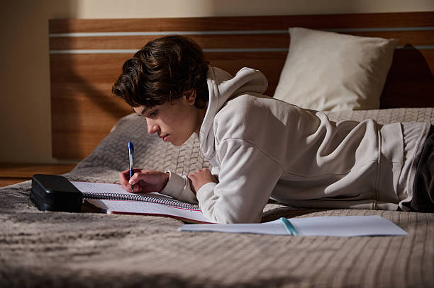 istock Student Lying on Bed Studying With Notebook and Pen in Cozy Bedroom 2251751721