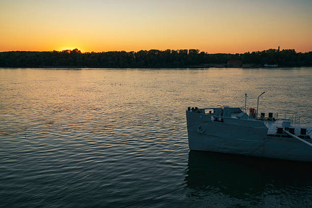 A peaceful sunset view over the Danube River in Ruse, Bulgaria, with the fading orange glow behind the distant treeline and a moored white ship gently resting on the calm evening waters.