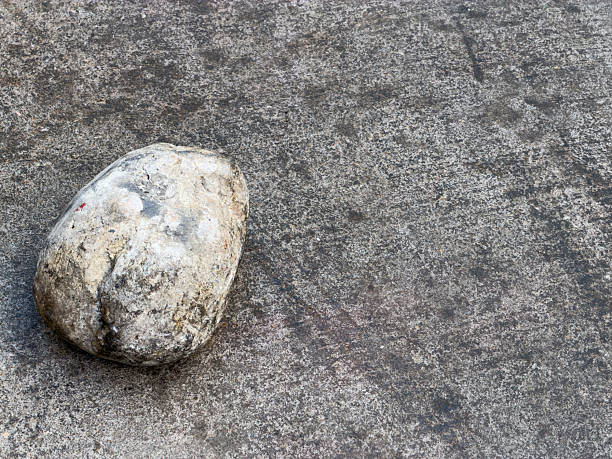 Rough gray stone pebble laying on textured concrete surface, creating a simple natural background