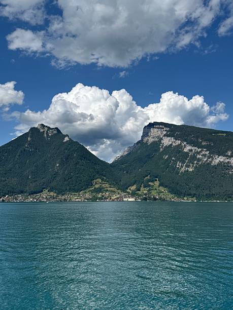 A clear view of Lake Thun with high mountain peaks rising behind the turquoise water, captured under bright summer clouds in Switzerland.
