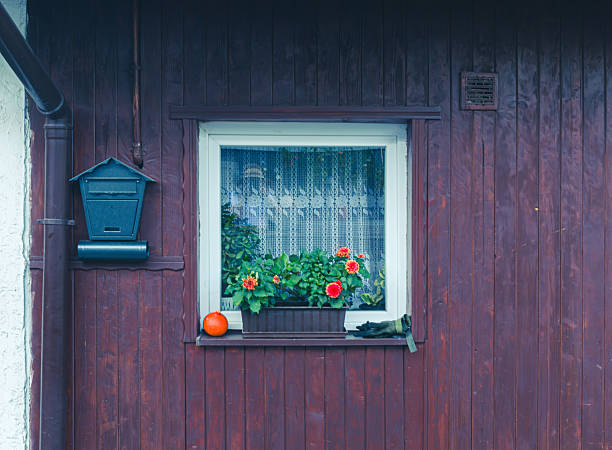 Lanckorona, Poland – August 19, 2025: Rustic wooden house facade featuring a small window with flower box, mailbox, and gardening gloves. Cozy countryside atmosphere reflecting rural life, home comfort, and traditional architecture.