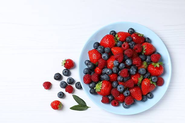 istock Different fresh ripe berries in bowl on light table, top view 2251768431