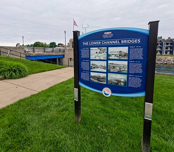 Charlevoix, Michigan, USA, June 24, 2025 : Informational sign explaining the history of the lower channel bridges. A double leaf bascule bridge is in the background of view.