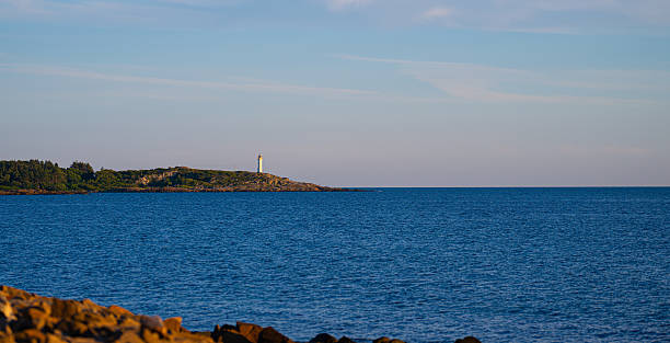 istock Coastal lighthouse on rocky shoreline under calm evening sky. 2251774958