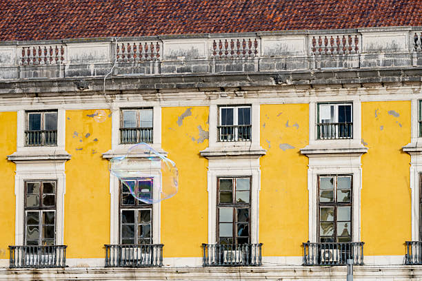 Several small soap bubbles float across a bright winter sky above historic yellow buildings in a Lisbon square