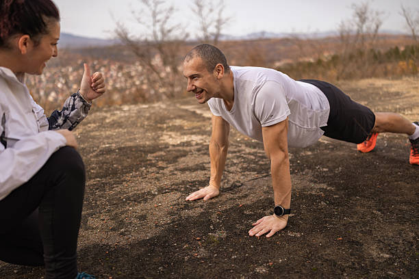 istock Sports trainer counting  and  providing guidance on proper push-ups  techniques while sports man exercising outdoor in the autumn. 2251782319