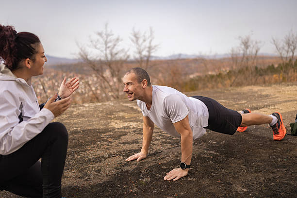 istock Sports trainer counting  and  providing guidance on proper push-ups  techniques while sports man exercising outdoor in the autumn. 2251782400