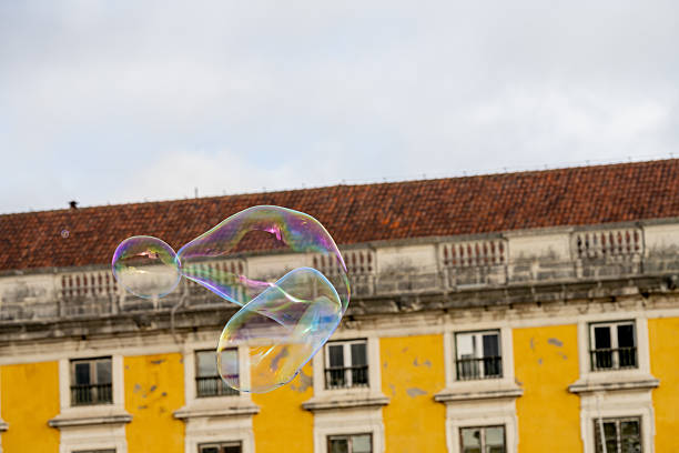 Lisbon Portugal December 05 2025. Soap bubbles float in front of a yellow historic building in the Alfama district during a winter afternoon.