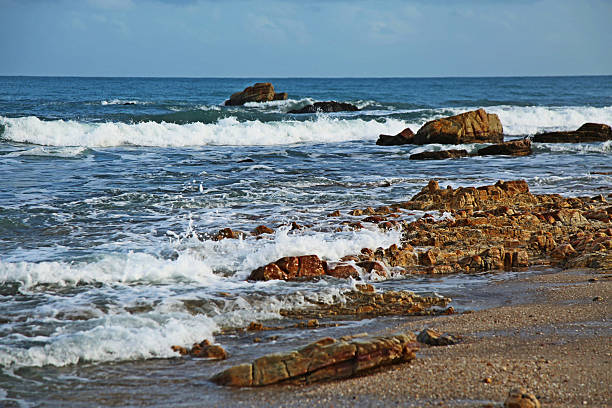 The coastline in Jericoacoara, Brazil, with rocks on the sand and the sea splashing over the stones.