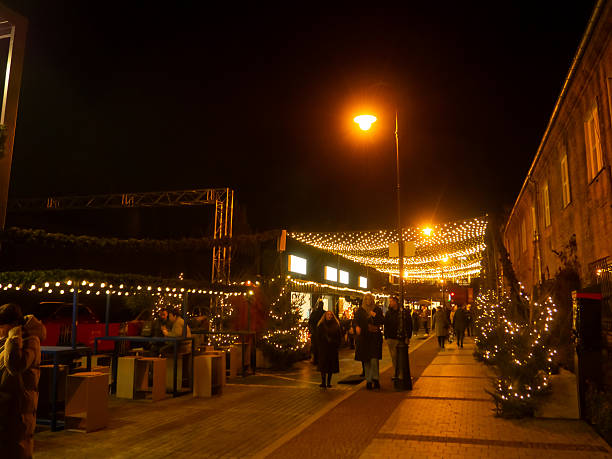 Gdansk, Old Town Centre – visitors walking through a cobblestone square featuring illuminated Christmas market stalls, decorated trees, and warm street lighting surrounded by historic buildings.