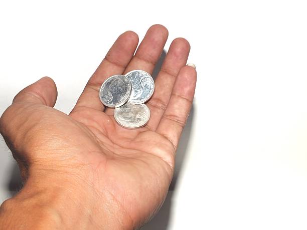 A hand holds three silver coins against a plain white background, highlighting the texture and simplicity of everyday currency.