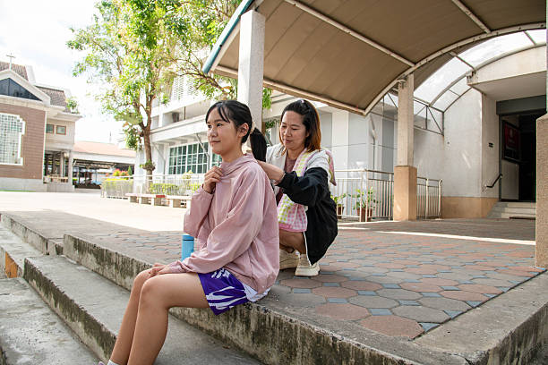 Two young Japanese women sit closely together outdoors in a peaceful park setting, sharing a quiet emotional moment as one friend gently comforts the other. The scene highlights empathy, emotional support, trust, and authentic friendship in everyday life. Natural light and relaxed surroundings create a warm, intimate atmosphere that reflects companionship, understanding, and human connection.