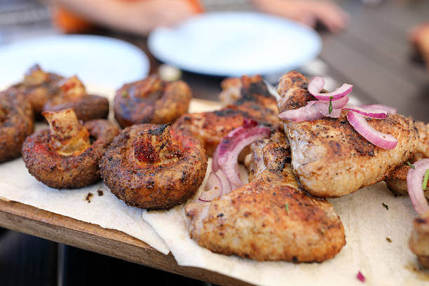 Grilled chicken drumsticks and mushrooms with red onion, freshly cooked on barbecue. Summer picnic, homemade food, outdoor cooking.