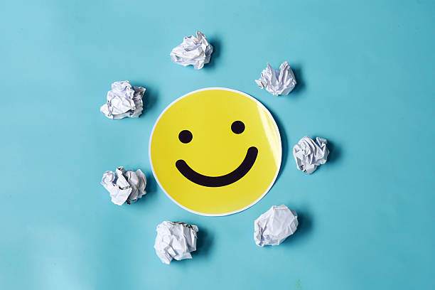 Optimistic yellow smiley face surrounded by rejected crumpled paper drafts on a vibrant blue backdrop, representing idea success, resilience, and positive feedback.