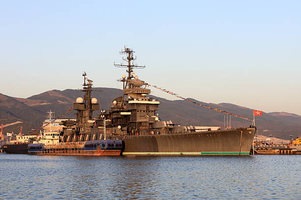 Large warship docked in port with mountains in background. Naval vessel for military and historical concept with clear sky.