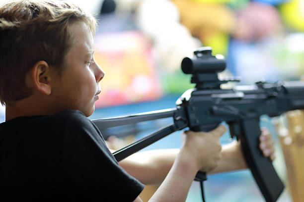 Boy playing shooting game with toy rifle at an amusement park. Child aiming a toy gun for target practice entertainment at a carnival.