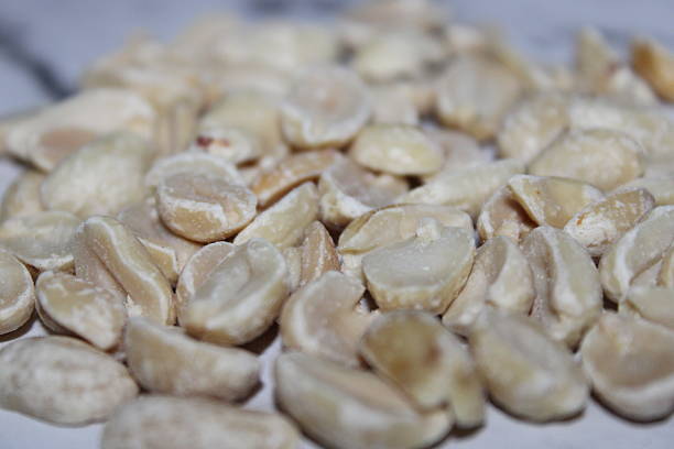 Peeled peanuts are spread out on a surface. These nuts are ready for cooking or can be used in various recipes. The setting is bright with natural light.