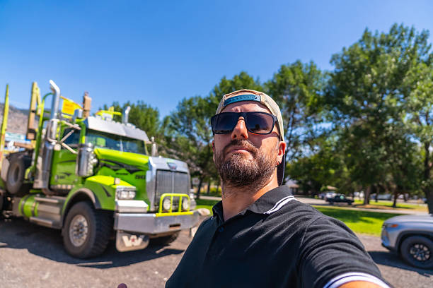 Trucker takes a selfie with his logging truck parked in a parking lot in kamloops, british columbia, on a sunny day, celebrating his job and the beauty of his surroundings