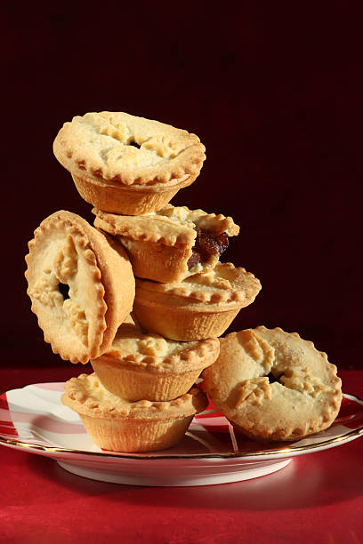 istock Close-up image of mince pie with missing bite on china plate containing stacked homemade mince pies on red surface, black background, focus on foreground 2251819528