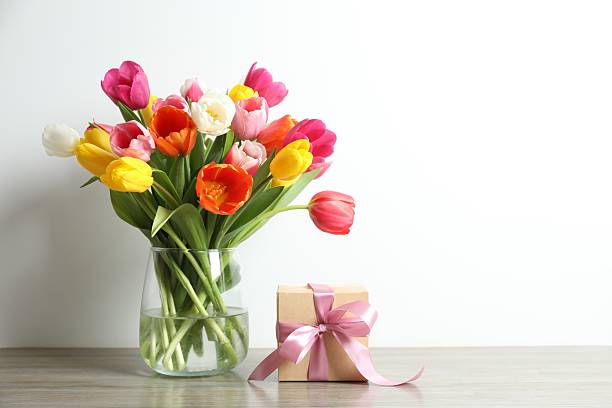 Beautiful fresh tulips in vase with gift box on table