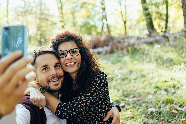Smiling mid adult couple embracing, taking a selfie in a sunlit forest